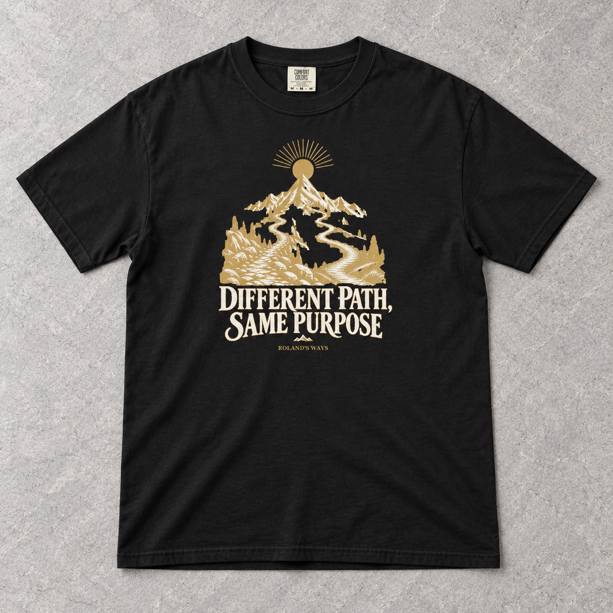 AI styled flat-lay mockup on slate: the black Different Path, Same Purpose T-shirt with gold and ivory mountain artwork.