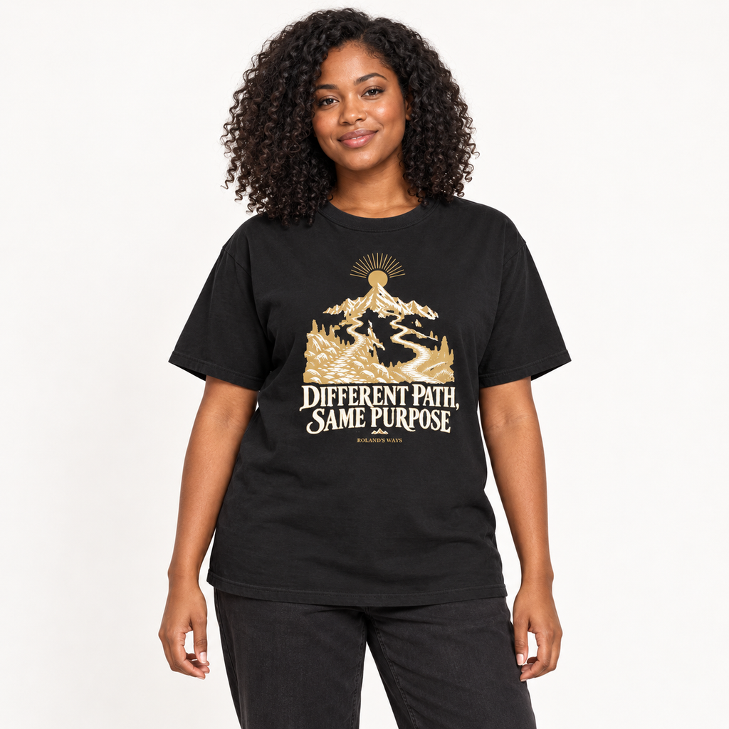 AI studio mockup of a woman wearing the black Different Path, Same Purpose T-shirt with gold and ivory mountain artwork.