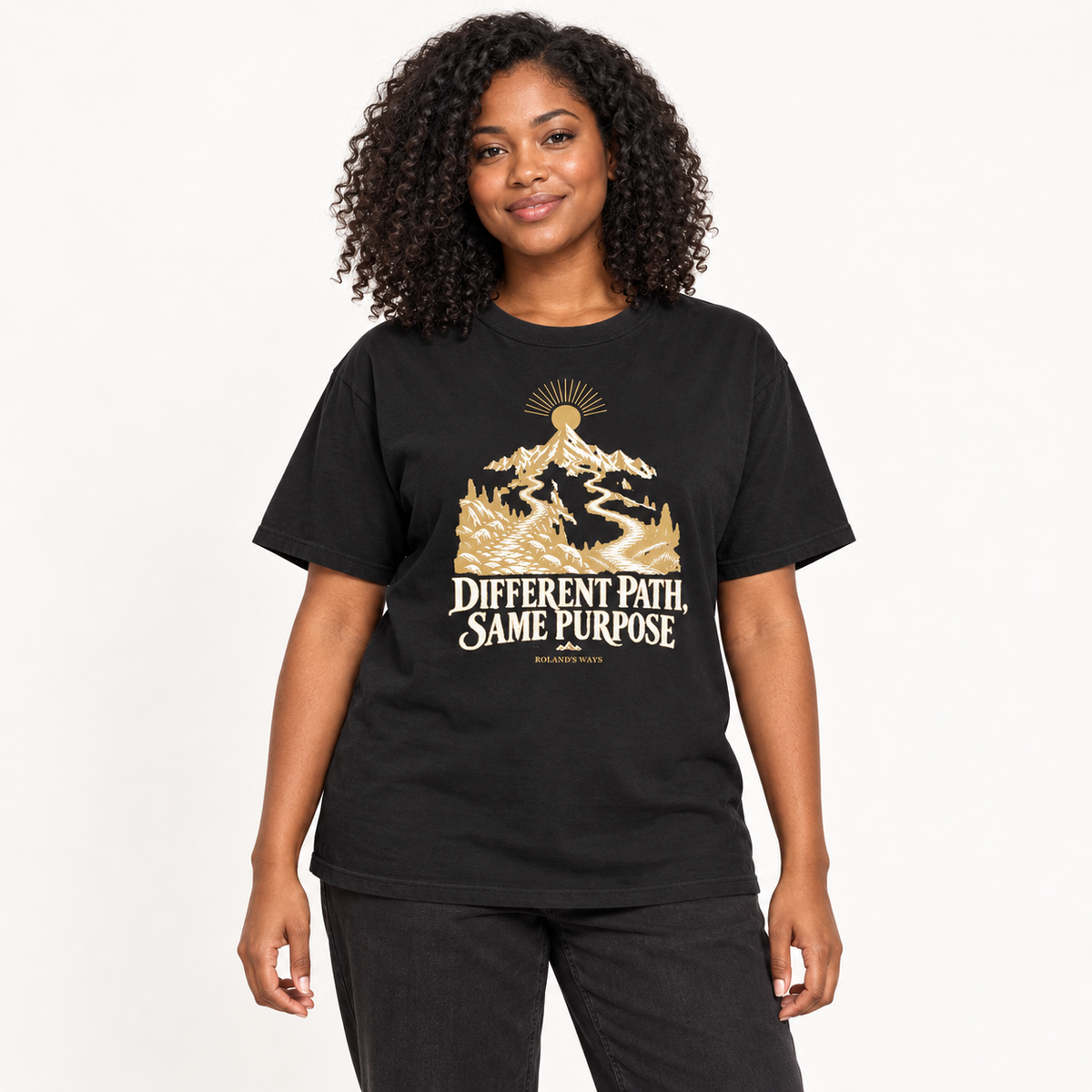 AI studio mockup of a woman wearing the black Different Path, Same Purpose T-shirt with gold and ivory mountain artwork.
