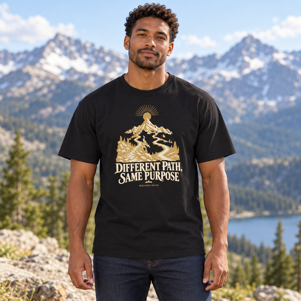 AI mountain lifestyle mockup of a man wearing the black Different Path, Same Purpose T-shirt with gold and ivory mountain artwork.