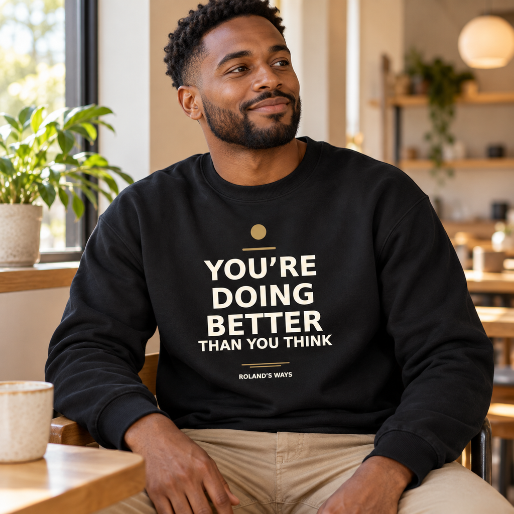 Model wearing the black You’re Doing Better Than You Think crewneck while seated at a café.