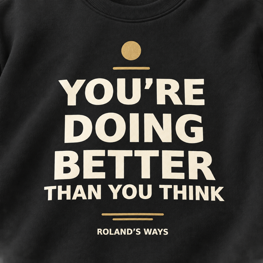 Close-up of You’re Doing Better Than You Think cream lettering and gold accents on the black crewneck.