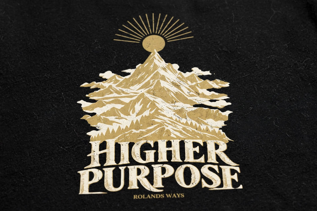 AI close-up mockup of the mountain artwork and slogan on the black Higher Purpose T-shirt with gold and ivory mountain artwork.